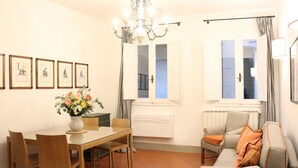 Ein Essbereich mit Tisch und Stühlen, einer Couch, einer Deckenleuchte und gerahmten Bildern an der Wand.