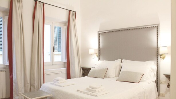 Ein Hotelzimmer mit einem großen Bett, zwei Nachttischen, einem Kopfteil und einem Fenster mit Vorhängen.