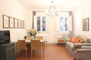 Ein Wohnzimmer mit Essbereich, einer Couch, einem Fernseher und gerahmten Bildern an der Wand.