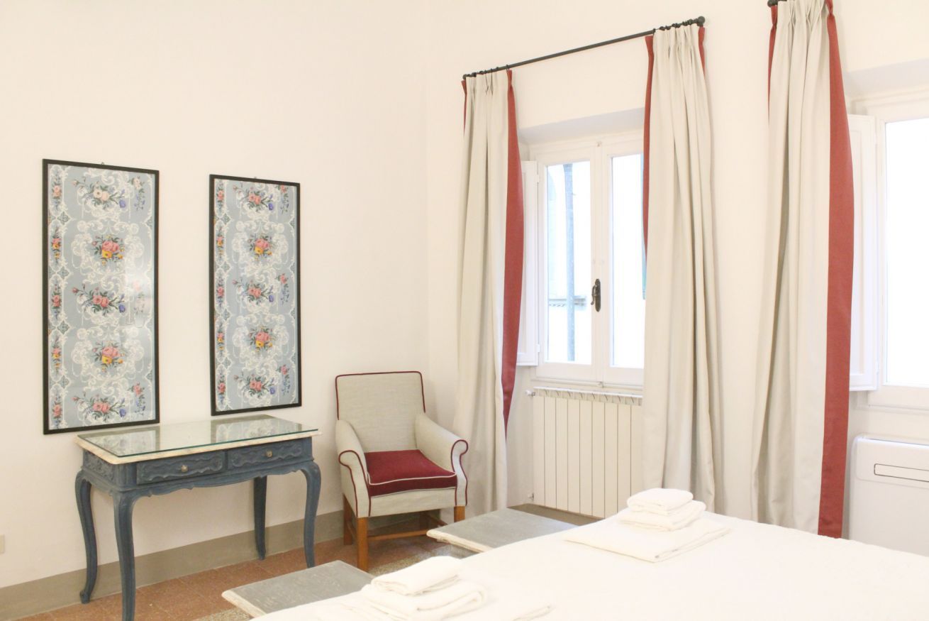 A room with a bed, a chair, a table, and two framed pictures on the wall.
