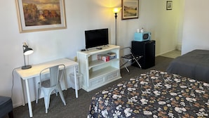 Habitación de hotel con escritorio, silla, cama y dos cuadros en las paredes.