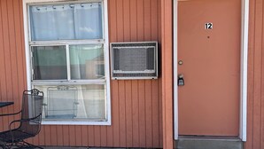 Un motel con una habitación individual, número 12, una ventana con mosquitero y una silla afuera.
