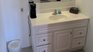 Un baño con tocador blanco, espejo, lavamanos y toallero.