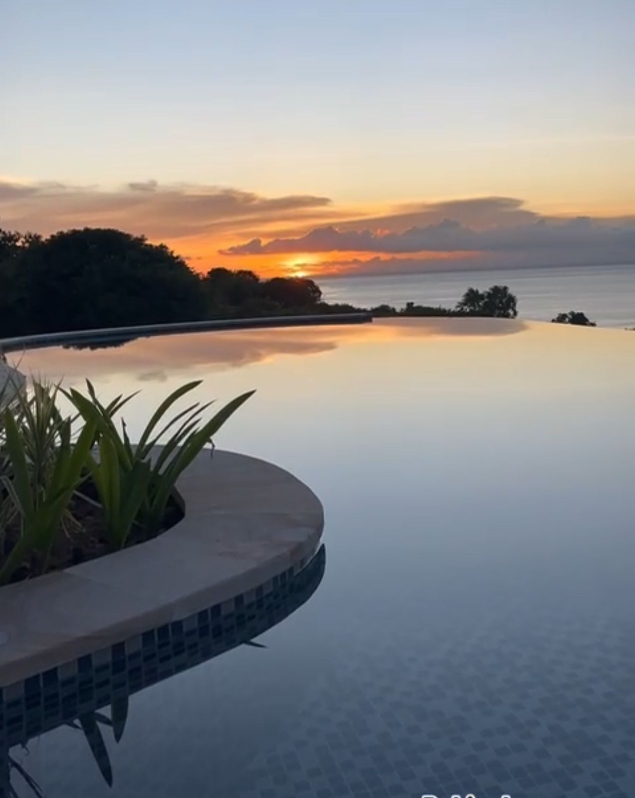 A serene infinity pool with a clear view of the sunset over the water.