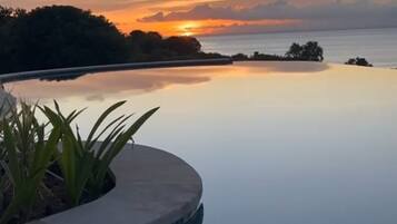 A serene infinity pool with a clear view of the sunset over the water.