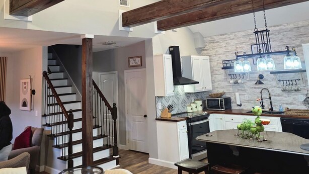 Una cocina moderna con vigas de madera, un comedor con mesa de vidrio y una escalera que sube a otro nivel.