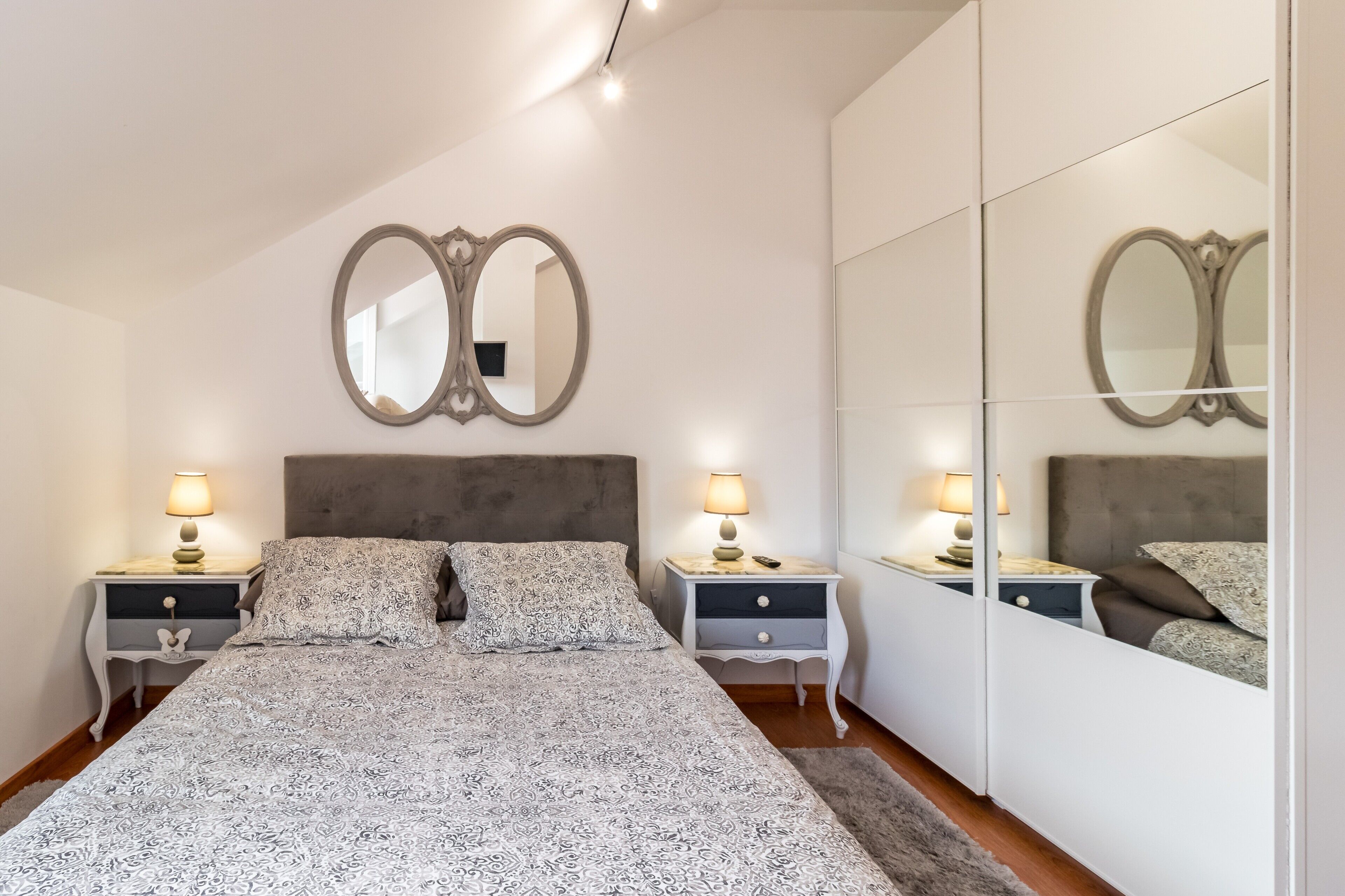 A bedroom with a bed, two bedside tables with lamps, a large mirror, and a wardrobe.