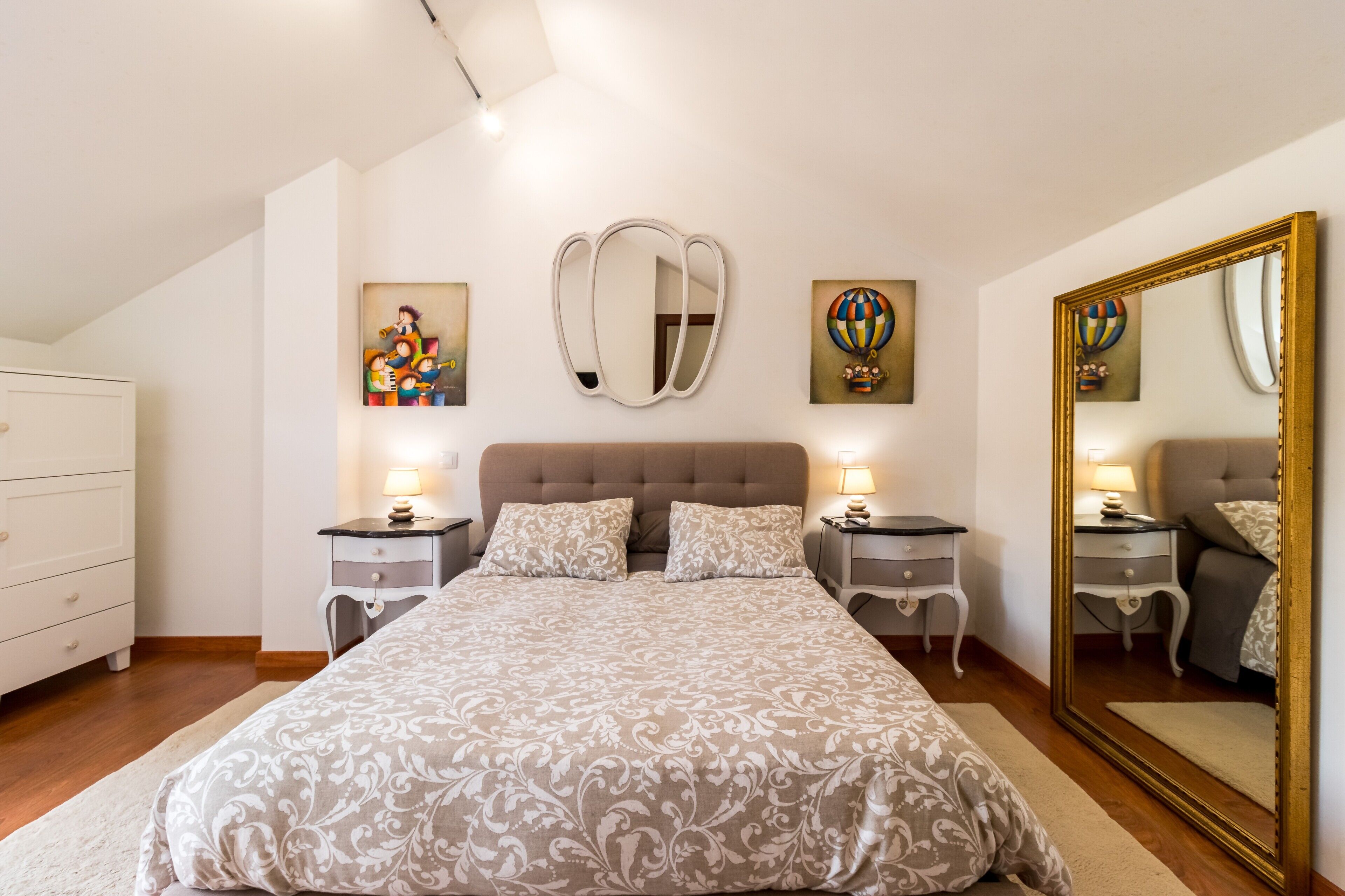 Un dormitorio con una cama grande, dos mesitas de noche, un aparador y un espejo grande.