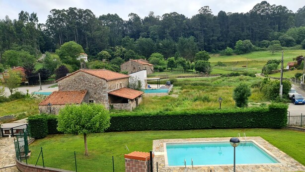 Ein Steingebäude mit Swimmingpool, umgeben von einer gepflegten Rasenfläche und einem bewaldeten Hügel im Hintergrund.