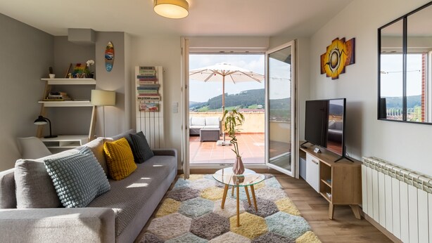 A living room with a sofa, TV, and a view through the glass door. - Apartment 'Luminoso' with Mountain View, Private Terrace and Wi-Fi (Renedo de Piélagos)