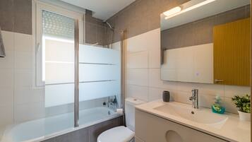 Un baño moderno con ducha envuelta en vidrio, inodoro, lavamanos con espejo y una planta en maceta.