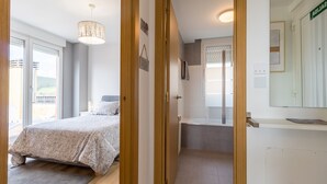 A bedroom with a bed, a bedside table, a nightstand, a window, and a door leading to a bathroom. - Apartment 'Luminoso' with Mountain View, Private Terrace and Wi-Fi (Renedo de Piélagos)