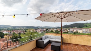 A rooftop terrace with a sofa, table, umbrella, and string lights. - Apartment 'Luminoso' with Mountain View, Private Terrace and Wi-Fi (Renedo de Piélagos)
