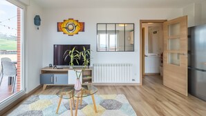 A modern living room with a TV, plants, and a glass table. - Apartment 'Luminoso' with Mountain View, Private Terrace and Wi-Fi (Renedo de Piélagos)