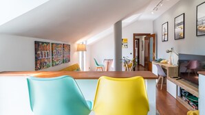 Una cocina moderna con encimera de madera, dos sillas coloridas y una zona de comedor con mesa y sillas.