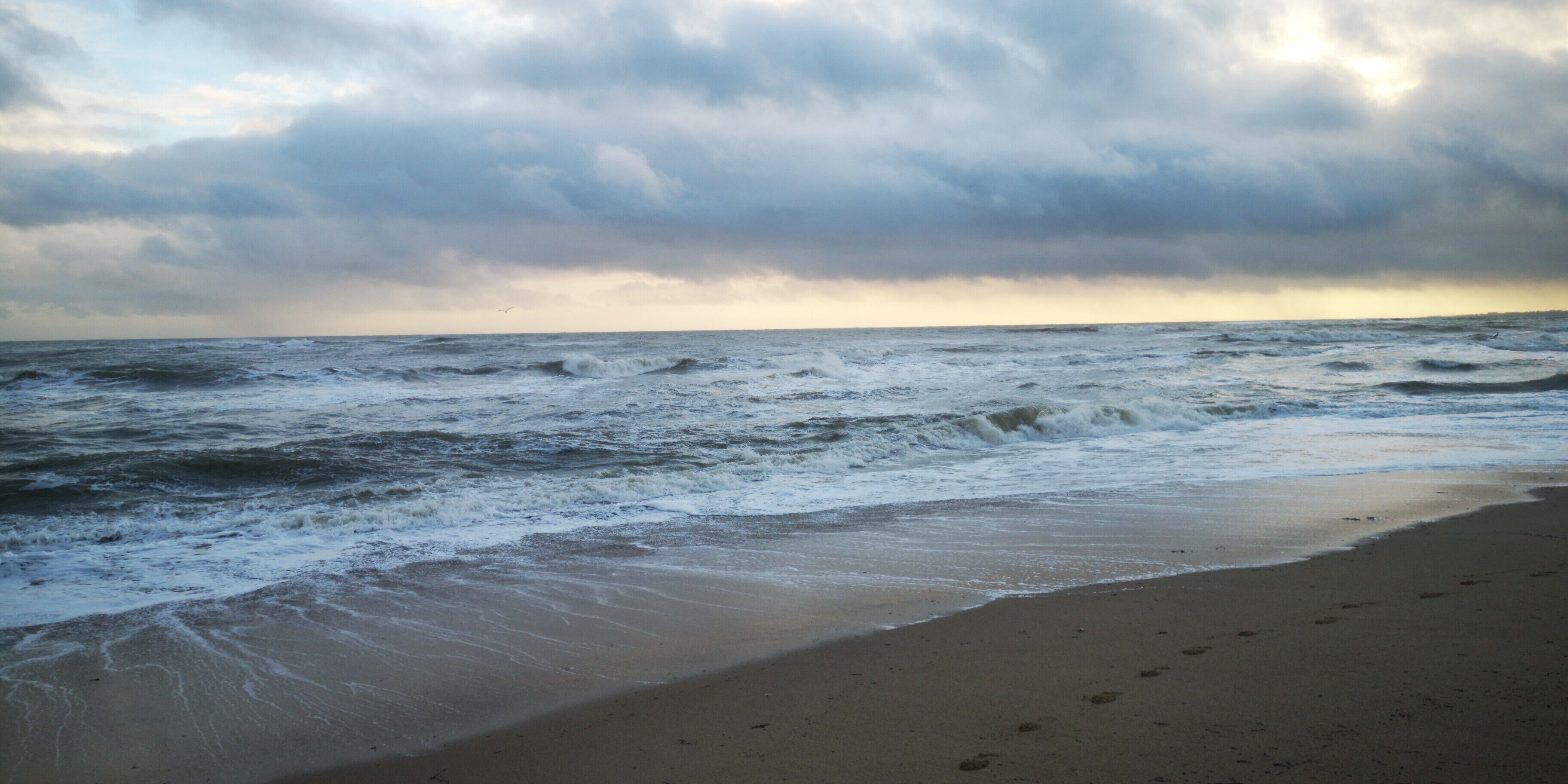 Ein Strand mit Wellen, bewölktem Himmel und weiter Ferne.