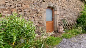 Un edificio de piedra con puerta de madera, muro de piedra y cerca de madera.