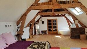 Dormitorio estilo loft con vigas de madera a la vista, una cama grande, un tapete colorido y un tragaluz.