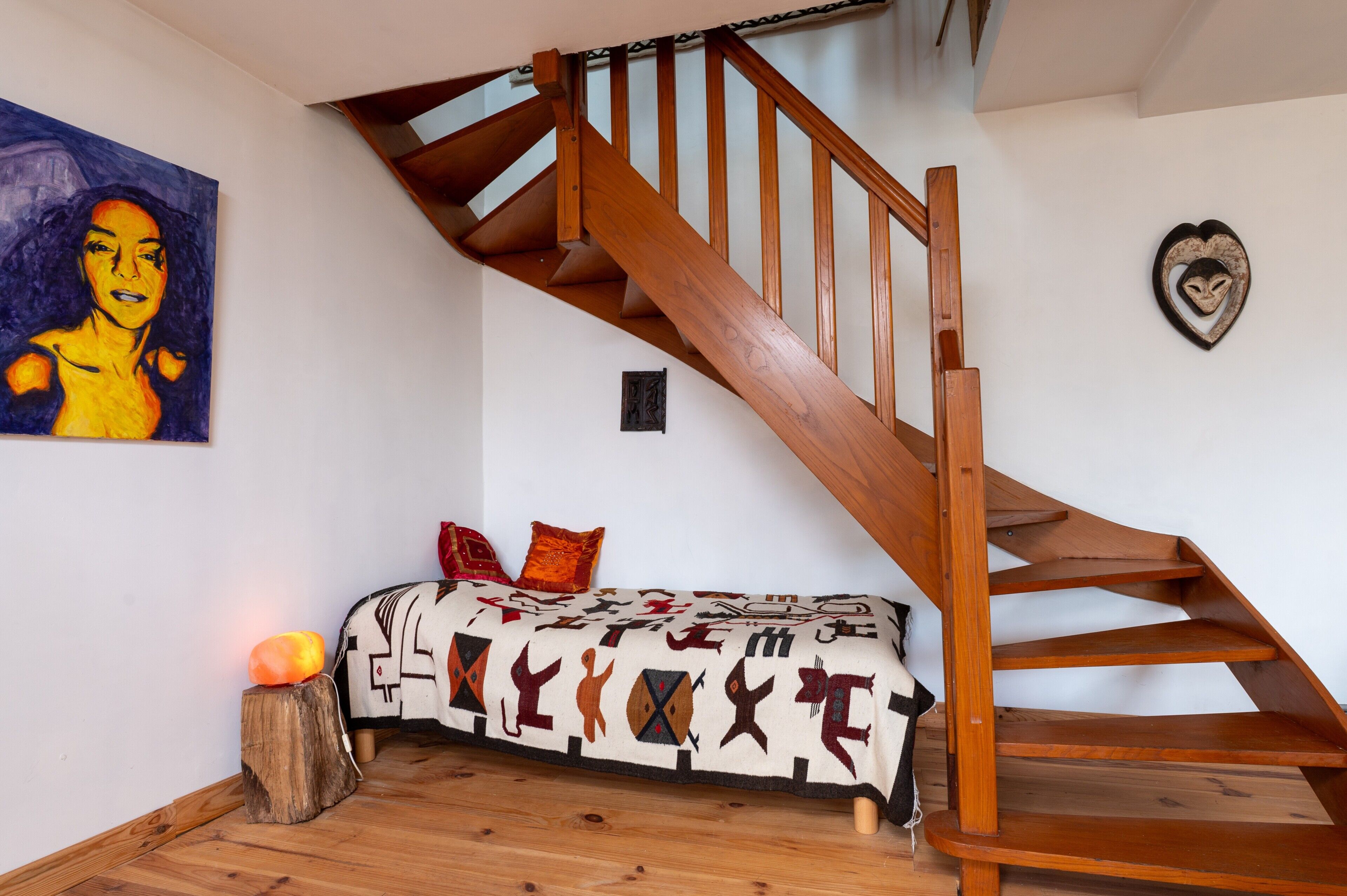 Un escalier en bois, un canapé avec des coussins à motifs et un tableau accroché au mur.