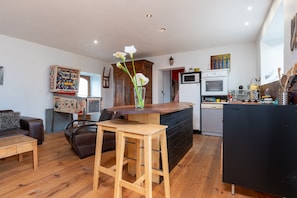 Une cuisine moderne avec un îlot central en bois, un coin repas avec un tabouret de bar, et un salon avec un canapé et une table basse.