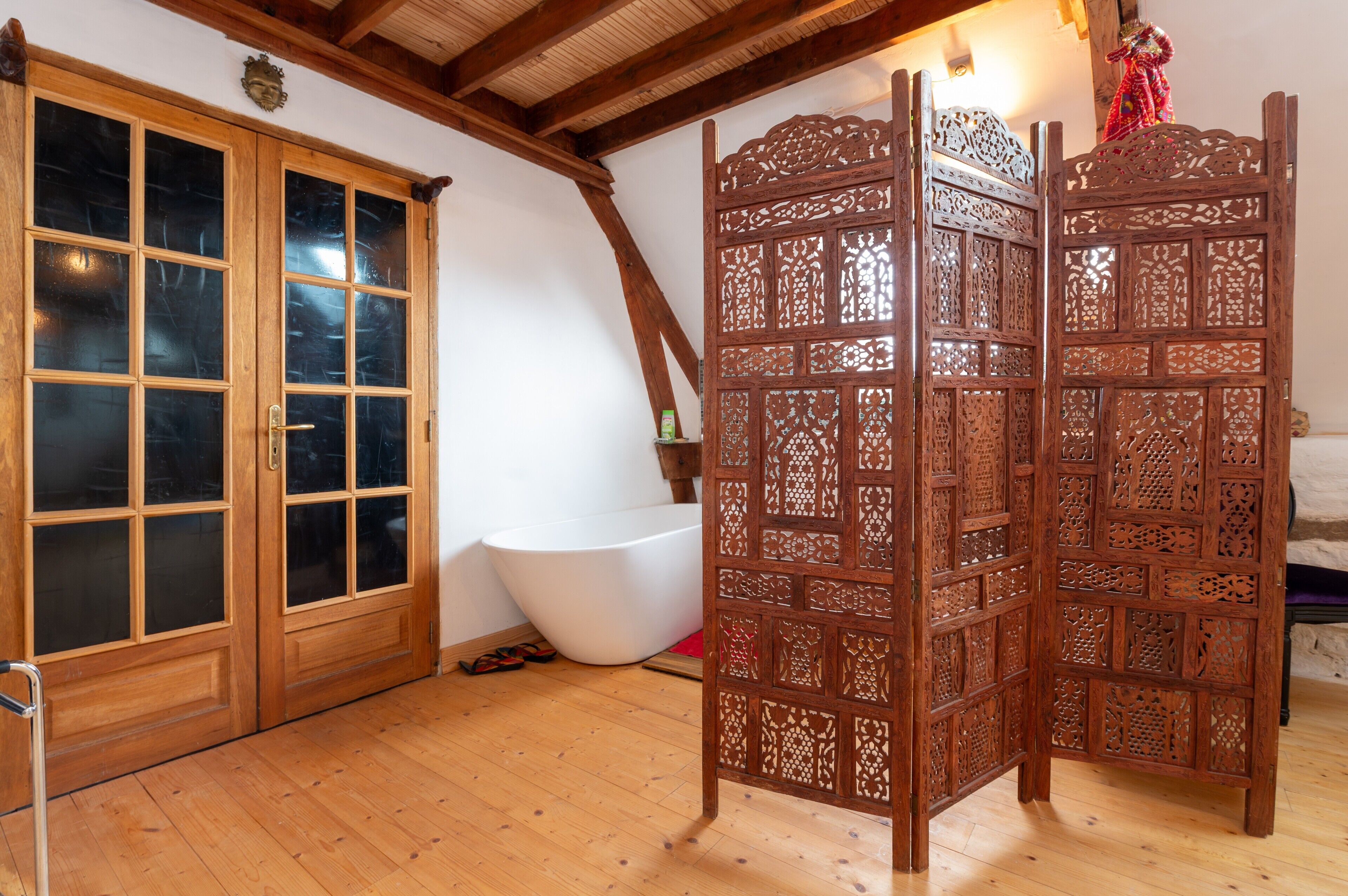 A room with wooden doors, a bathtub, and a decorative screen.