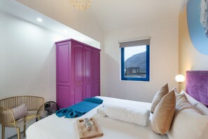 Un dormitorio con cama, una mesita de noche de madera, un armario púrpura, un ventanal con vista a la montaña y una lámpara fijada a la pared.