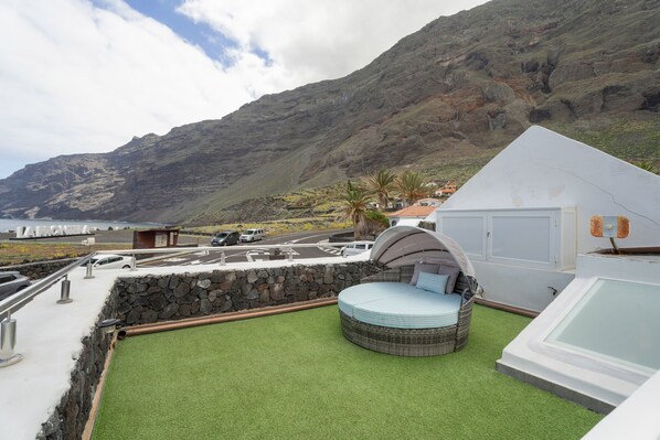Una terraza en la azotea con una zona de estar circular, un jacuzzi y vistas a un paisaje montañoso.