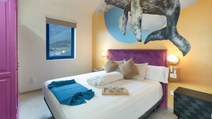 A hotel room with a bed, a large whale mural on the wall, a window with a view, and a pink door.