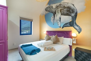 Habitación de hotel con una cama, un gran mural de una ballena en la pared, una ventana con vistas y una puerta rosa.