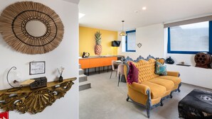 Ein modernes Wohnzimmer mit einem gelben Sofa, einem dekorativen Spiegel und einer Küche im Hintergrund.