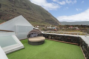 Terraza en la azotea con un área de estar circular, cerramiento de vidrio y vistas a un pueblo costero.