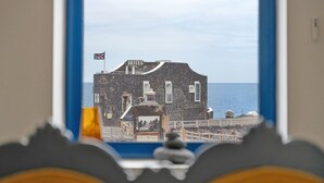 Blick auf ein Steingebäude mit einer Flagge, auf dem 'HOTEL' steht, durch ein Fenster mit blauem Rahmen.