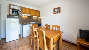 A compact kitchen with a dining table, wooden cabinets, a refrigerator, and a microwave. - Apartment 'Neptune' with Mountain View and Balcony (Albiez-Montrond)