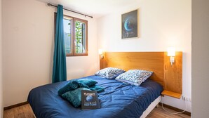 A bedroom with a wooden headboard, a bed with blue bedding, a window with curtains, a wall-mounted light, and a poster of Neptune. - Apartment 'Neptune' with Mountain View and Balcony (Albiez-Montrond)
