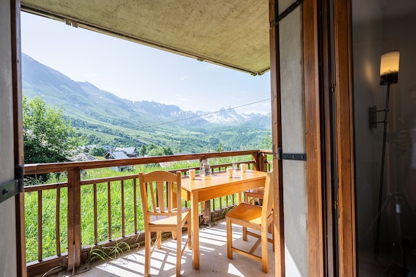 Un balcon avec une table et des chaises en bois, donnant sur un paysage montagneux.