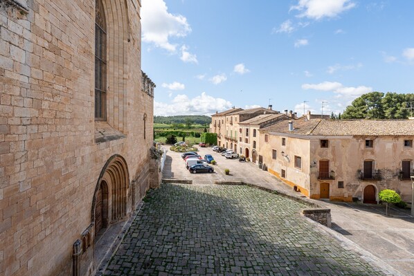 A cobblestone street leading to a building with a large arched entrance, surrounded by other buildings with tiled roofs.