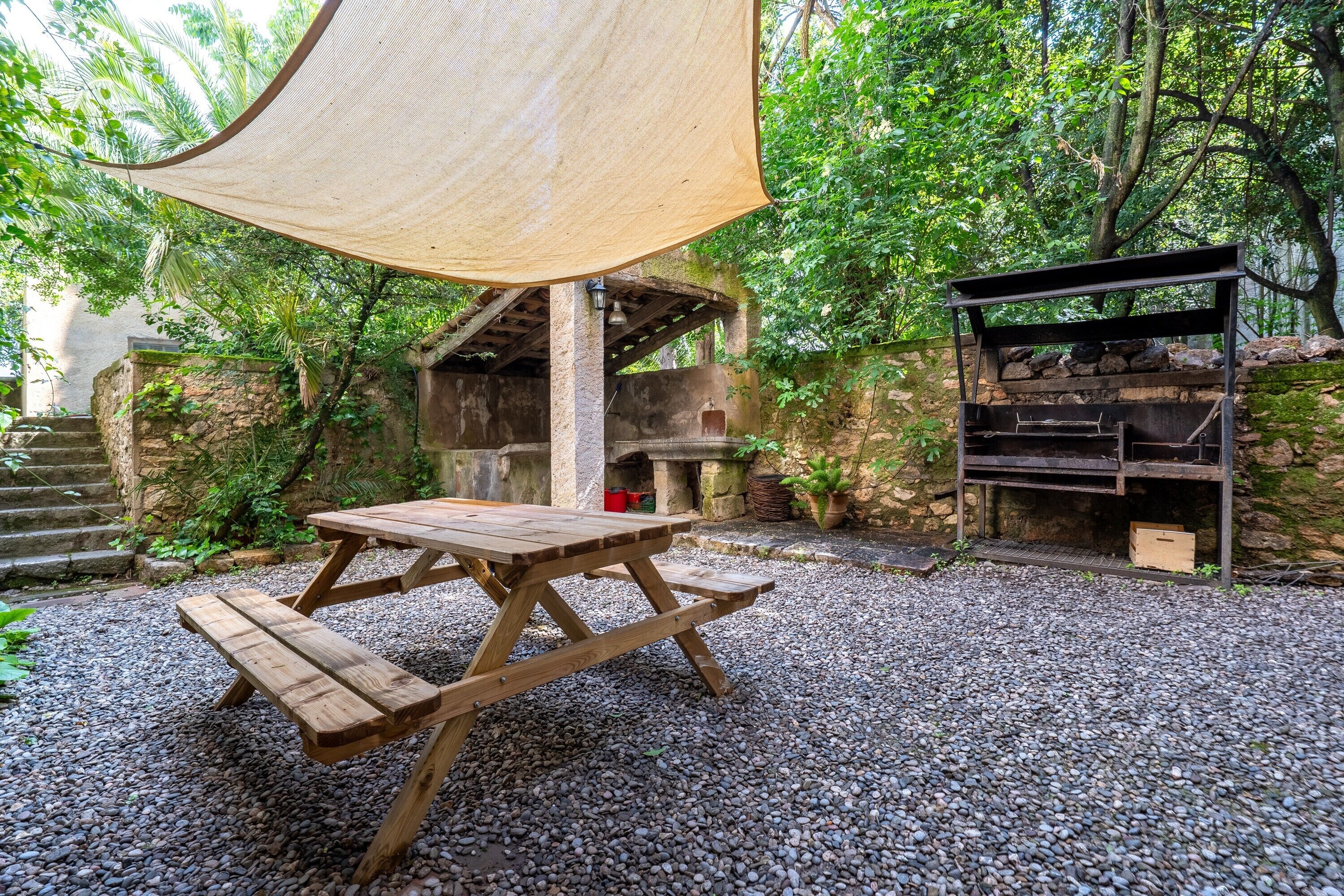 A wooden picnic table with benches, a barbecue grill, and a shaded area with a net.
