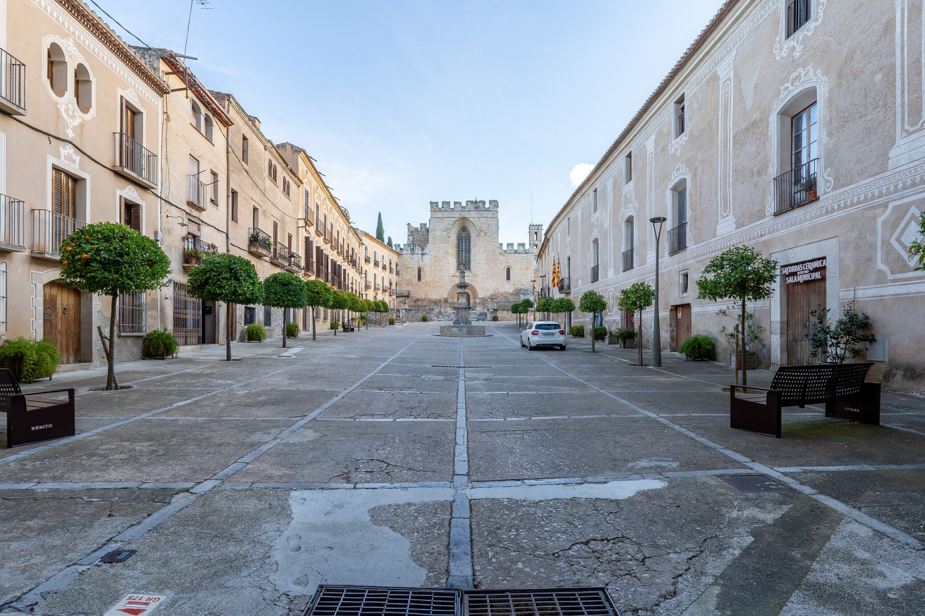 A street with historic buildings, a central fountain, and a castle-like structure in the distance.