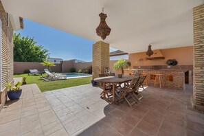Eine Außenpatio mit Pool, einem Holztisch und -stühlen, einer Ziegelstütze und einer hängenden Leuchte.