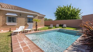 A swimming pool with lounge chairs, a brick house, and a green lawn.