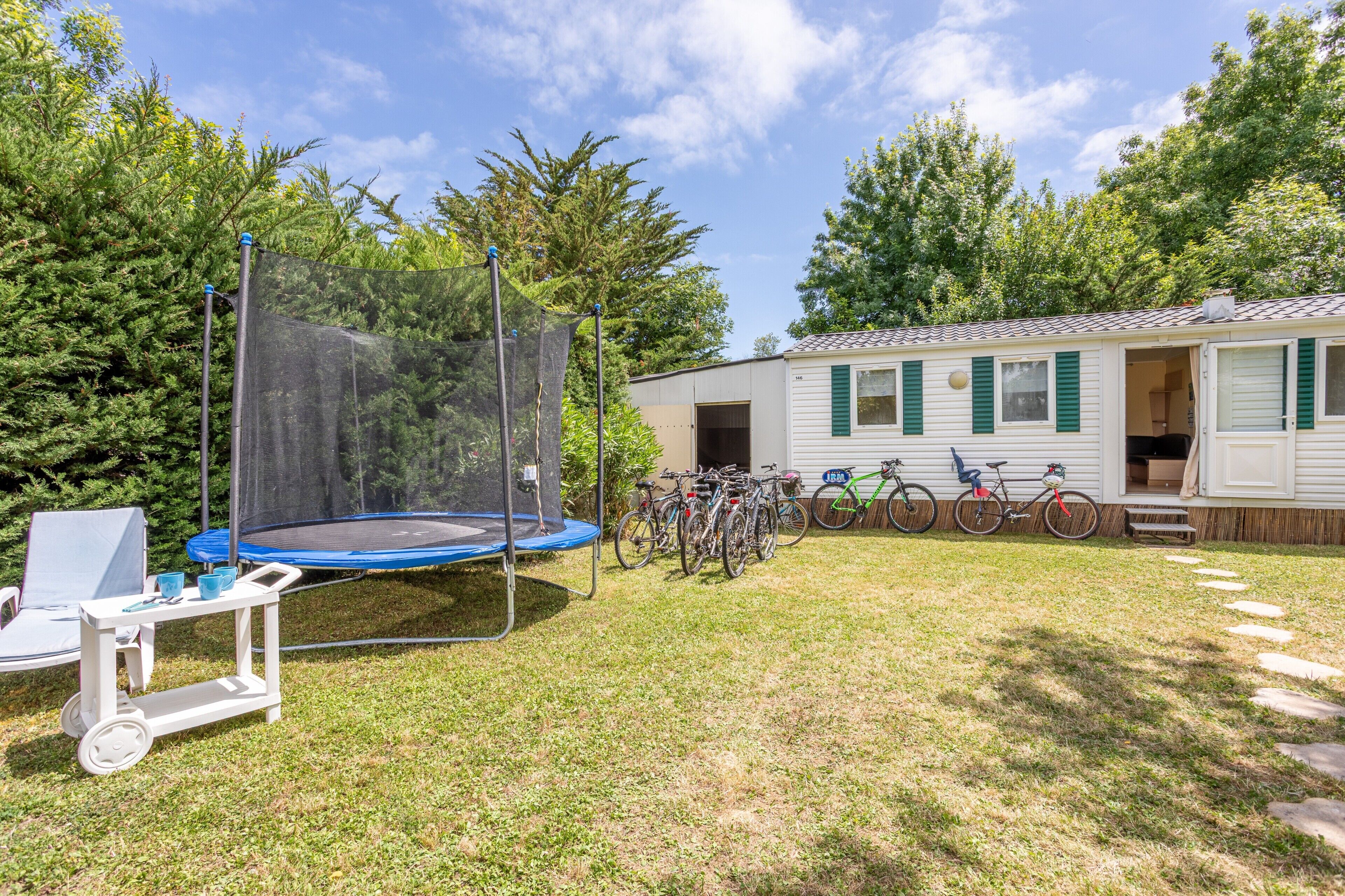 A house with a trampoline, bicycles, and a small outdoor seating area.