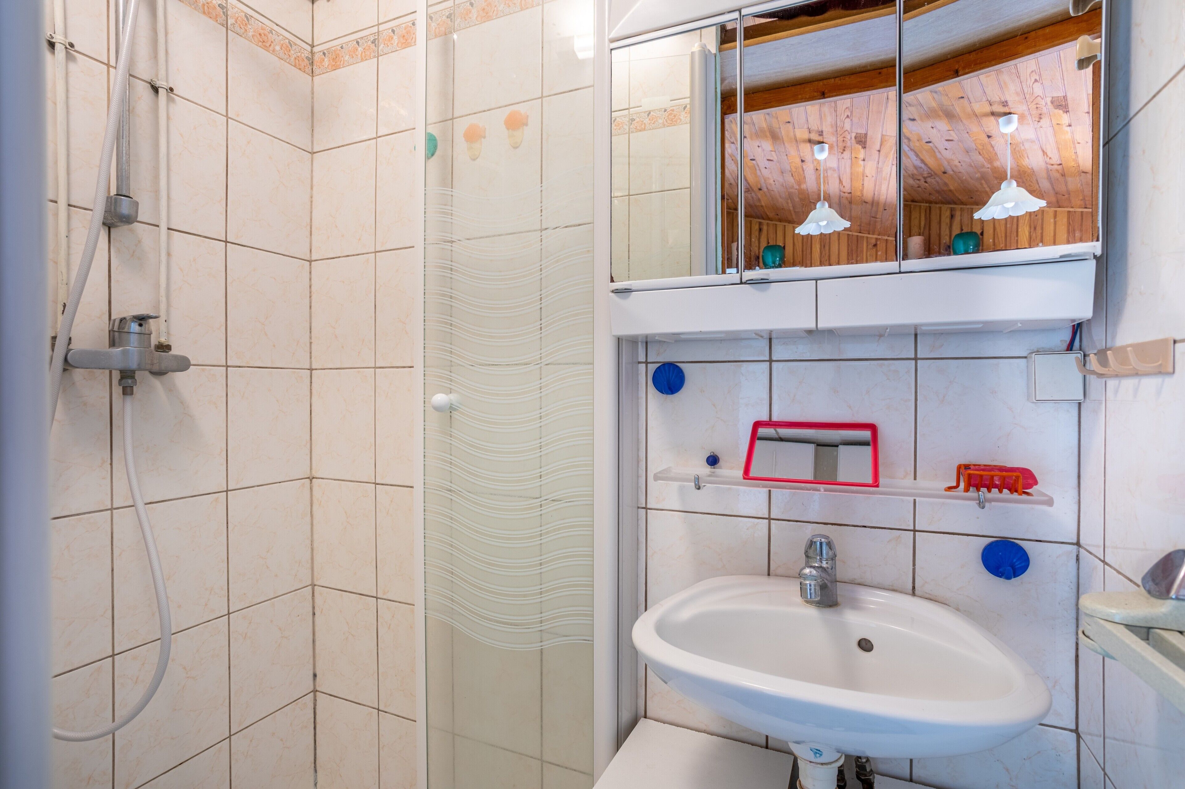 A bathroom with a shower, a sink, a mirror, and a shelf with toiletries.