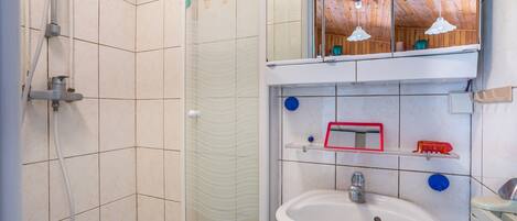 A bathroom with a shower, a sink, a mirror, and a shelf with toiletries.