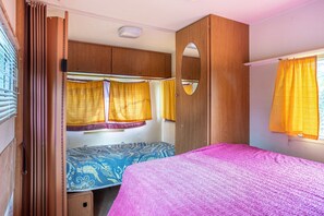 Un dormitorio compacto para casa rodante con una cama litera, una cama individual, un armario de madera y un espejo.