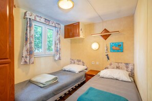 A small, cozy room with two beds, a window with curtains, a wall-mounted cabinet, and a picture.