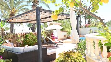 An outdoor patio with a pergola, lounge chairs, a sofa, and a pool.