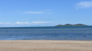 Une plage avec une eau d’un bleu limpide et des collines qui se dessinent à l’horizon.