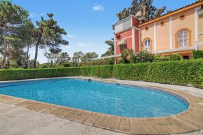 A swimming pool with a tiled edge, surrounded by a hedge and trees. - Apartment 'Mirador Del Golf' with Shared Pool, Private Terrace and Wi-Fi (Islantilla)