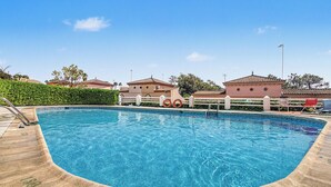 A swimming pool with a wooden deck, surrounded by buildings with tiled roofs.