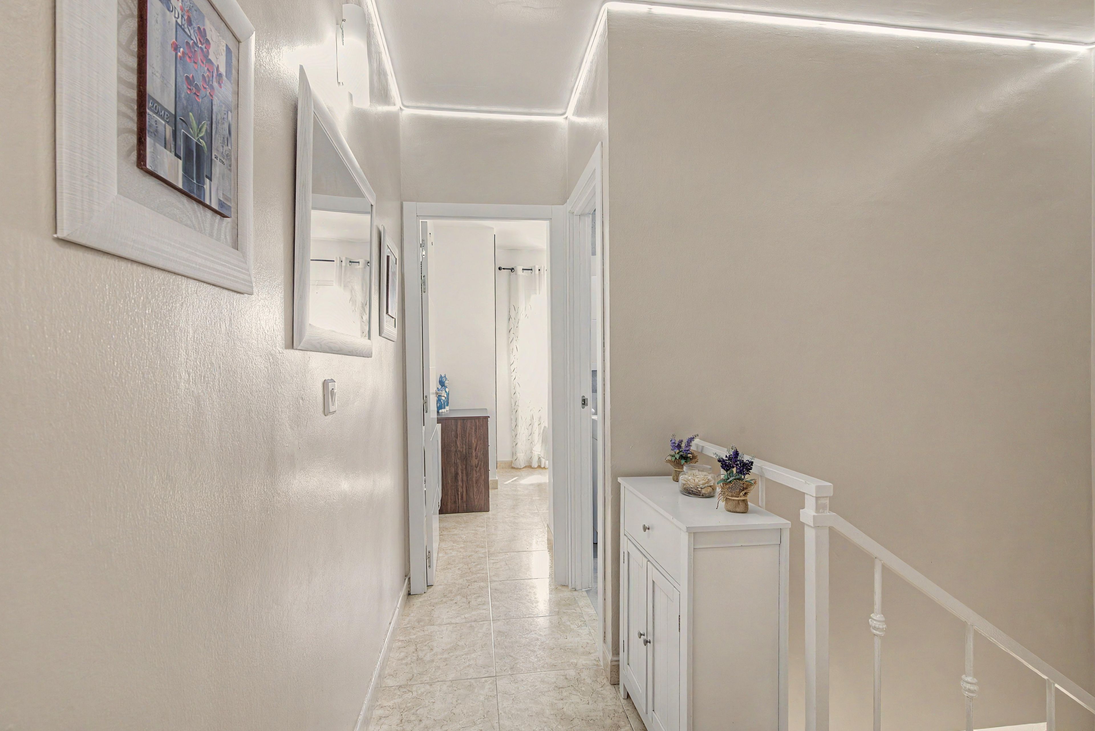 Un pasillo con una puerta blanca, un mueble pequeño y un cuadro en la pared.